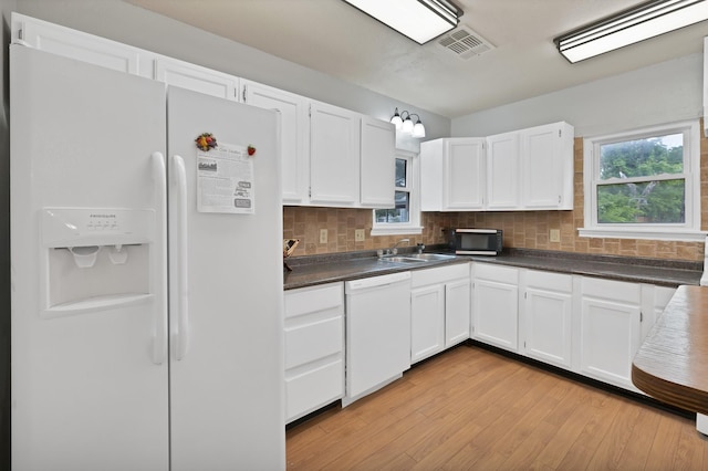 kitchen with white appliances, white cabinets, dark countertops, and a sink