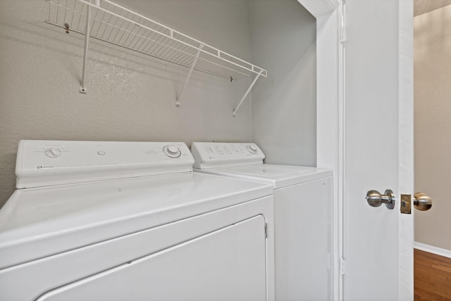 clothes washing area with washing machine and clothes dryer, baseboards, wood finished floors, and laundry area