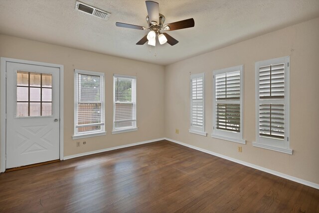 spare room featuring baseboards, ceiling fan, dark wood-type flooring, and visible vents