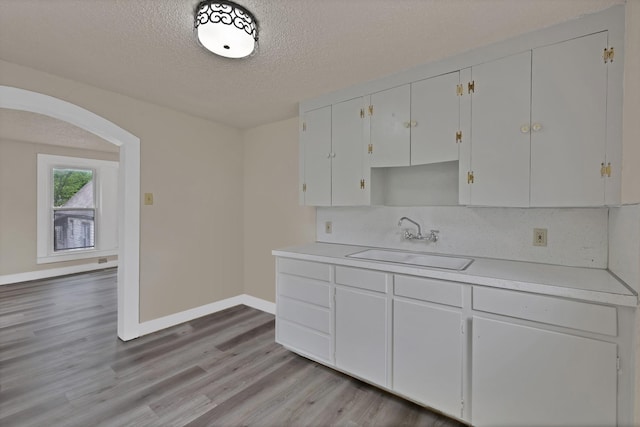 kitchen with a sink, light wood-style floors, light countertops, arched walkways, and a textured ceiling
