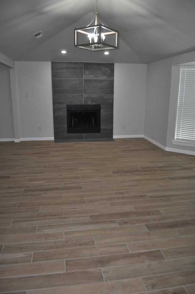 unfurnished living room with a tiled fireplace, baseboards, visible vents, lofted ceiling, and wood finished floors