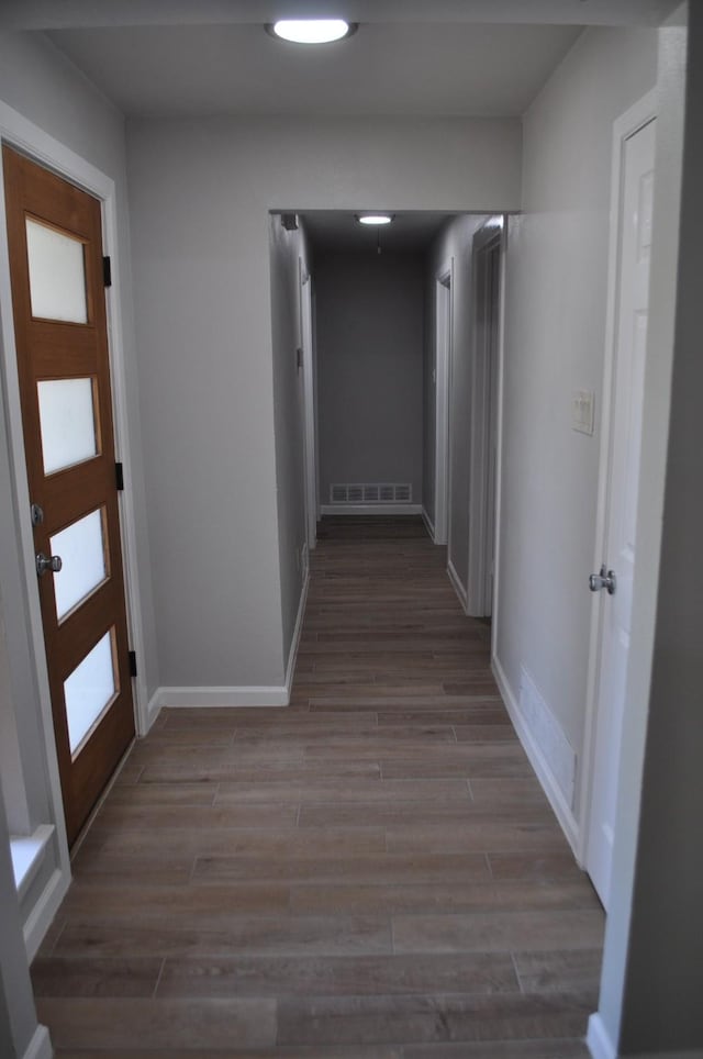 corridor featuring baseboards, wood finished floors, and visible vents