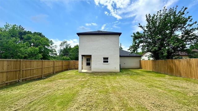 back of house featuring a fenced backyard, brick siding, and a yard