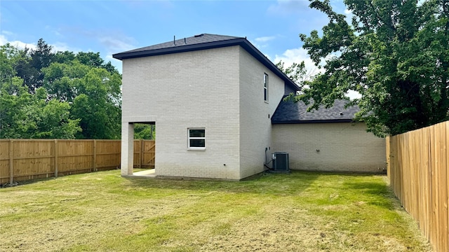 back of house with a fenced backyard, brick siding, a yard, and cooling unit