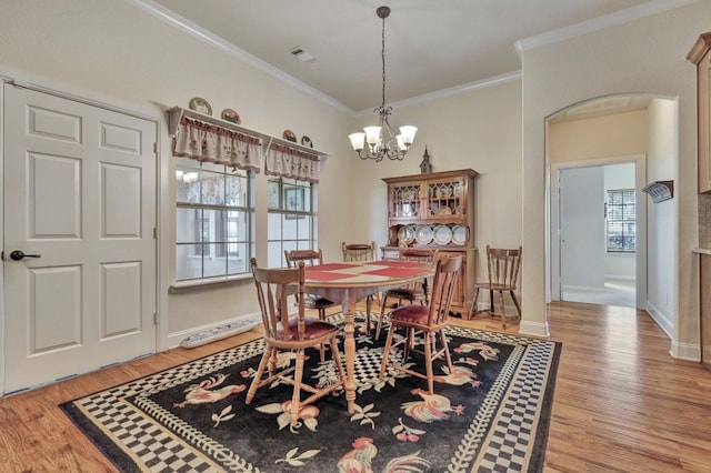 dining area with light wood-style flooring, arched walkways, visible vents, an inviting chandelier, and ornamental molding