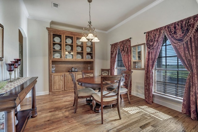 dining room with arched walkways, light wood-type flooring, baseboards, visible vents, and ornamental molding
