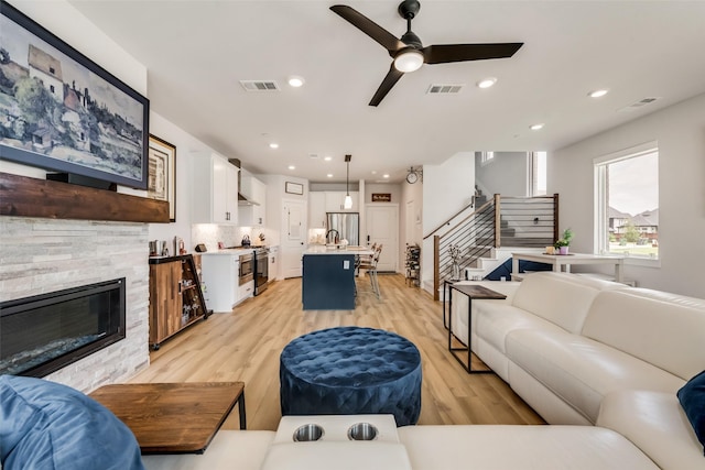 720 Bandera Ct, Prosper, TX 75078 - living area featuring stairway, a stone fireplace, visible vents, a ceiling fan, and light wood-type flooring