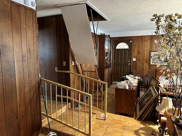 entrance foyer with wooden walls, a textured ceiling, and stairs