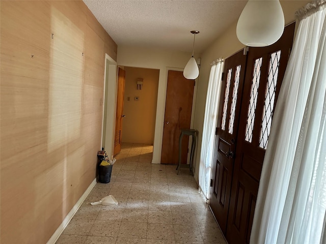 corridor featuring a textured ceiling, baseboards, and light floors