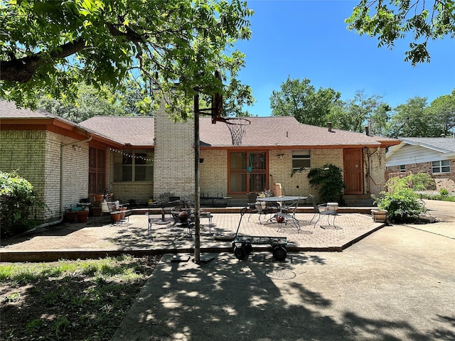 back of house featuring a chimney, brick siding, roof with shingles, and a patio