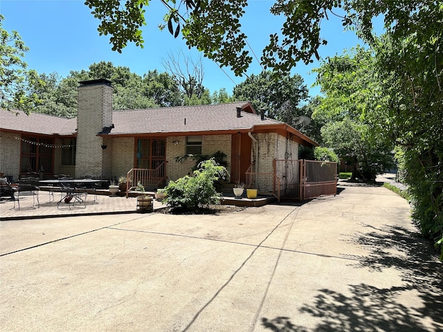 back of property featuring a chimney, brick siding, roof with shingles, and a patio