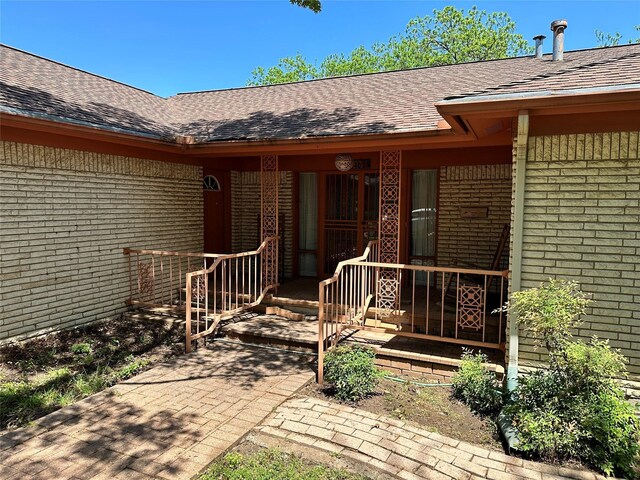 view of exterior entry featuring brick siding and roof with shingles