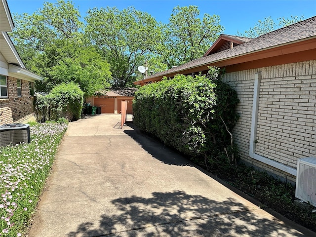view of property exterior featuring brick siding, roof with shingles, a patio, and central AC unit