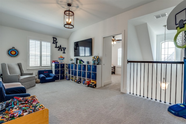 recreation room featuring carpet, visible vents, lofted ceiling, and ceiling fan with notable chandelier