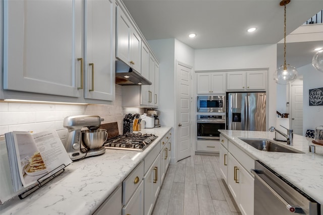 kitchen with light stone counters, a sink, decorative backsplash, appliances with stainless steel finishes, and under cabinet range hood