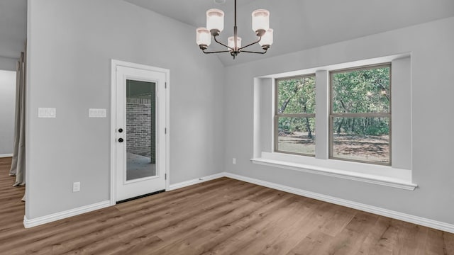 unfurnished dining area featuring wood finished floors, baseboards, an inviting chandelier, and vaulted ceiling