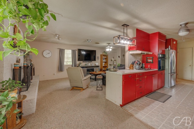 kitchen featuring cooktop, under cabinet range hood, red cabinets, freestanding refrigerator, and black oven