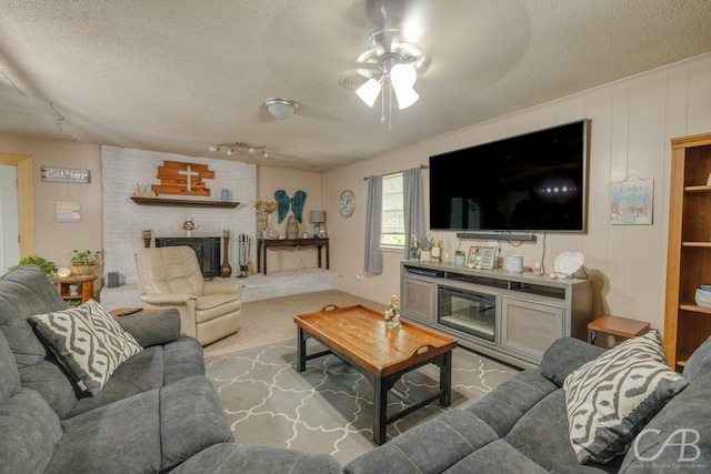 living room featuring carpet flooring, a ceiling fan, a brick fireplace, and a textured ceiling