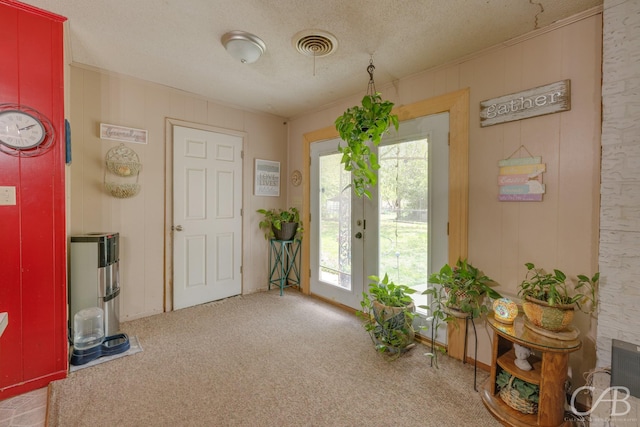 carpeted entrance foyer with crown molding, a textured ceiling, visible vents, and a healthy amount of sunlight