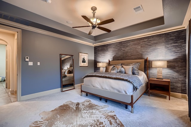 carpeted bedroom with ceiling fan, arched walkways, a tray ceiling, baseboards, and visible vents