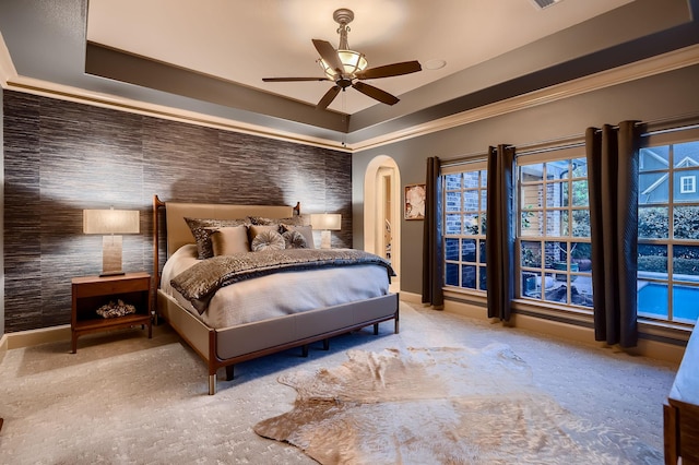 carpeted bedroom featuring crown molding, ceiling fan, arched walkways, a raised ceiling, and baseboards