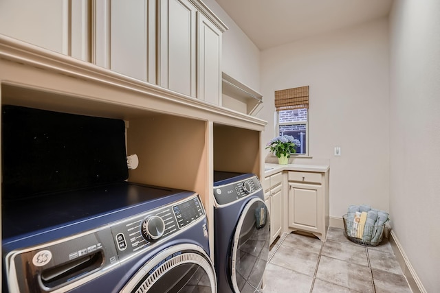 clothes washing area featuring light tile patterned flooring, baseboards, washing machine and clothes dryer, and cabinet space