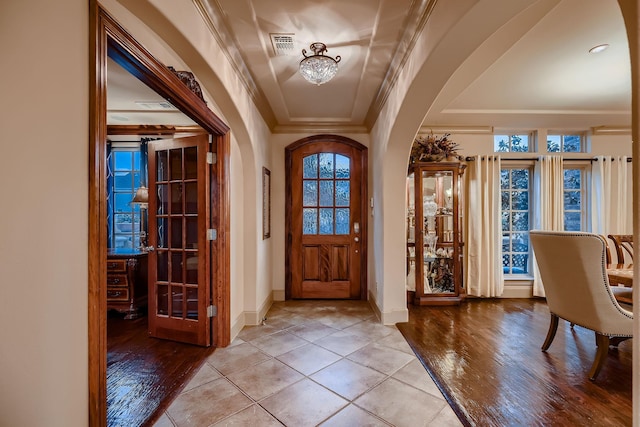 entrance foyer with light wood-style floors, arched walkways, baseboards, ornamental molding, and visible vents