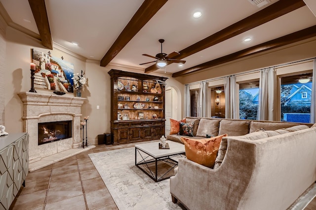 living area with tile patterned floors, ceiling fan, arched walkways, beamed ceiling, and a premium fireplace
