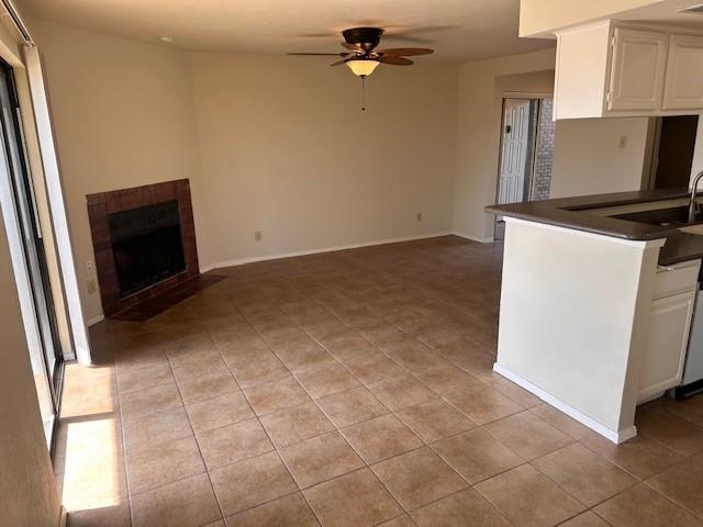 4544 Chaha Rd Unit 103, Garland, TX 75043 - kitchen with dark countertops, a ceiling fan, a tiled fireplace, and white cabinetry