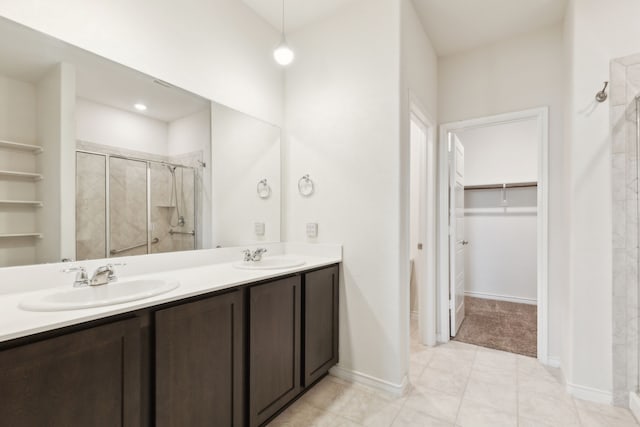 bathroom with a walk in closet, a sink, double vanity, and a stall shower