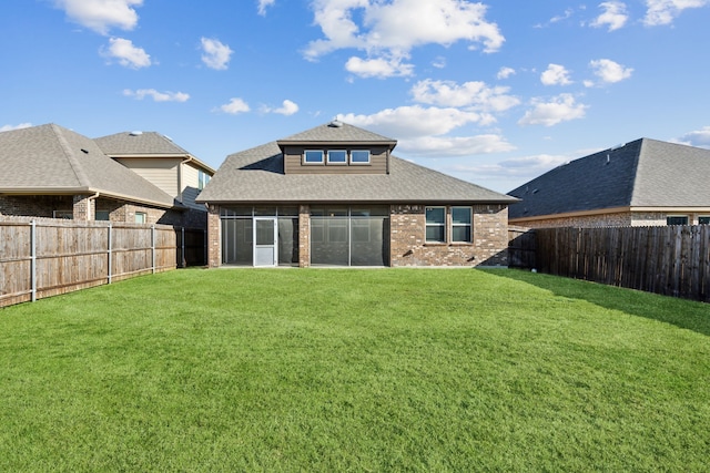 rear view of property featuring a fenced backyard, a sunroom, brick siding, and a yard