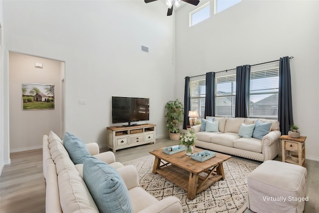 living area with light wood finished floors, baseboards, visible vents, a ceiling fan, and a high ceiling