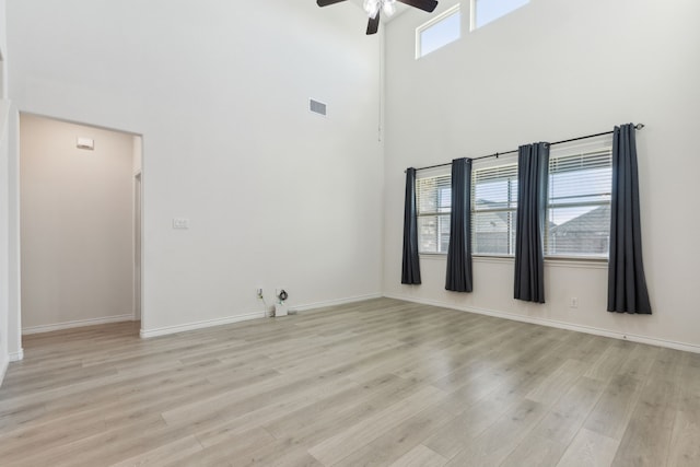unfurnished room with a towering ceiling, visible vents, a ceiling fan, baseboards, and light wood-style flooring