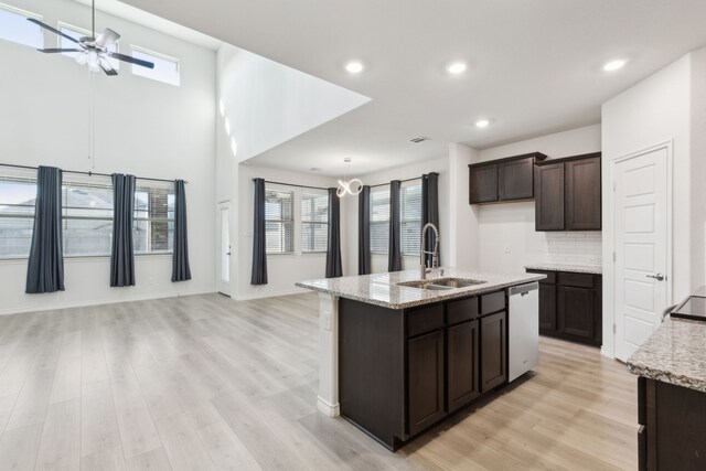 kitchen with light wood finished floors, dark brown cabinets, stainless steel dishwasher, a sink, and open floor plan