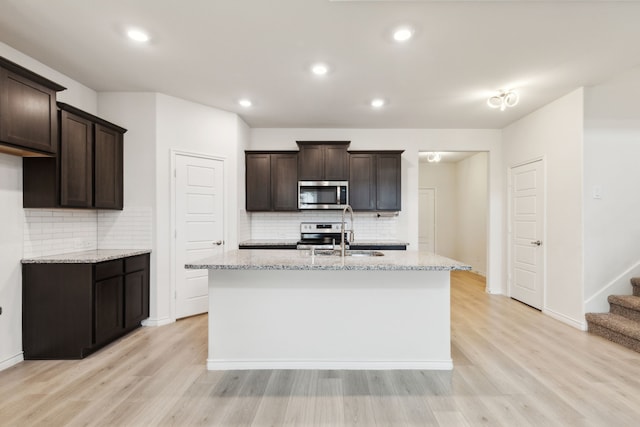 kitchen with a sink, dark brown cabinets, light wood-style floors, backsplash, and appliances with stainless steel finishes