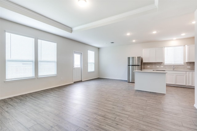 kitchen featuring a center island, decorative backsplash, light countertops, ornamental molding, and freestanding refrigerator