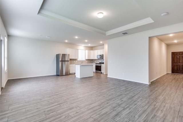 unfurnished living room with a tray ceiling, light wood-style floors, visible vents, and crown molding