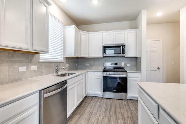 kitchen with white cabinets, a sink, light wood-style flooring, tasteful backsplash, and appliances with stainless steel finishes