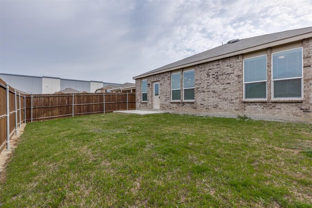 rear view of house featuring a fenced backyard, brick siding, a patio, and a lawn