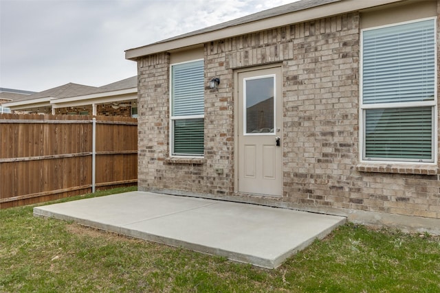 entrance to property featuring brick siding, fence, and a patio