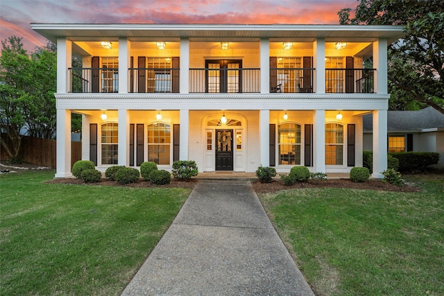 neoclassical home featuring a lawn, a porch, and a balcony