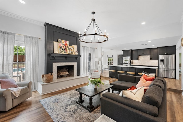 living room featuring a high end fireplace, plenty of natural light, crown molding, and an inviting chandelier