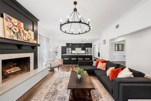 living room featuring crown molding, wood finished floors, an inviting chandelier, a premium fireplace, and visible vents