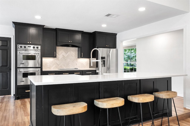 kitchen with stainless steel appliances, light wood-type flooring, visible vents, decorative backsplash, and light countertops