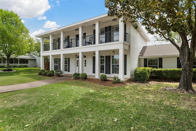 greek revival inspired property with brick siding, a porch, a front yard, and a balcony