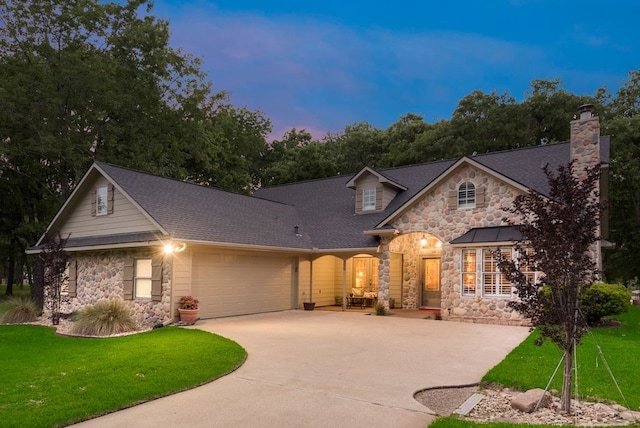 view of front facade featuring concrete driveway, a front lawn, stone siding, an attached garage, and roof with shingles