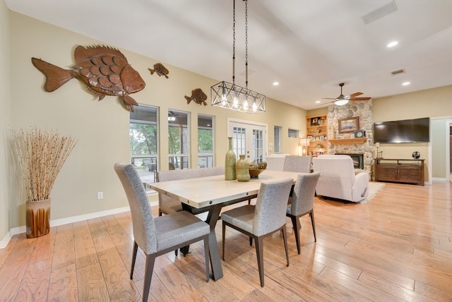 dining room with a ceiling fan, a stone fireplace, light wood-type flooring, baseboards, and recessed lighting