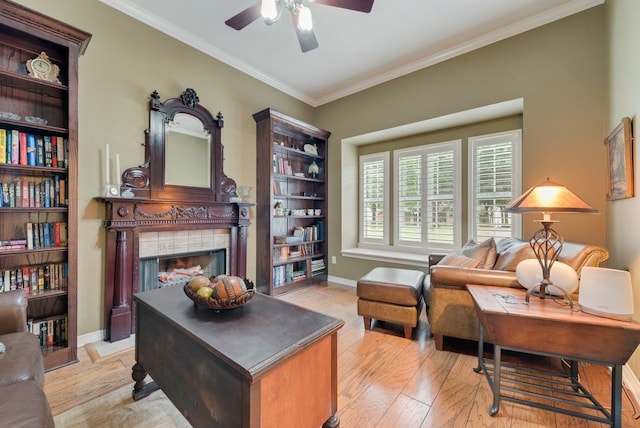 living area with a ceiling fan, light wood-style flooring, a fireplace, baseboards, and ornamental molding