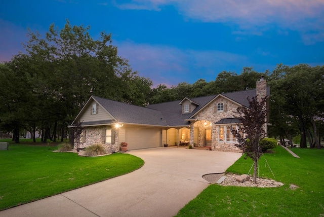 traditional home with a chimney, concrete driveway, an attached garage, stone siding, and a lawn