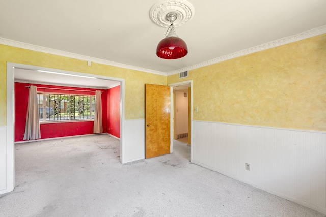 carpeted spare room with a wainscoted wall, visible vents, and ornamental molding